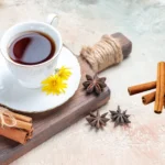 A steaming mug of cinnamon tea surrounded by cinnamon sticks, star anise on a wooden table.