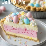 A slice of layered Eazy Pink Easter Jell-O Pie with pink, blue, and yellow layers, topped with whipped cream and pastel sprinkles.